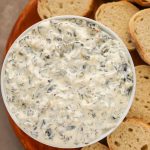 Close-up overhead view of a bowl of Keto Spinach Dip with baguette slices on the side.