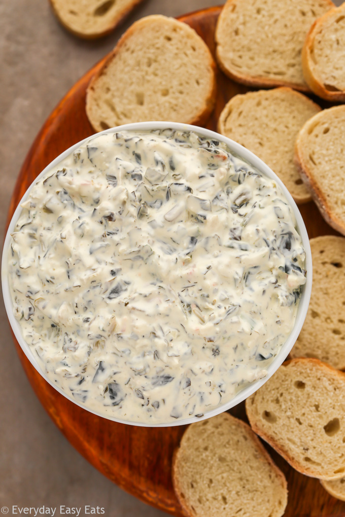 Close-up overhead view of a bowl of Keto Spinach Dip with baguette slices on the side.