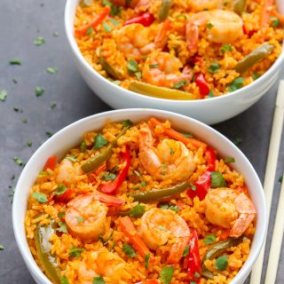 Overhead view of two bowls of Thai Shrimp and Rice with chopsticks on a black surface.