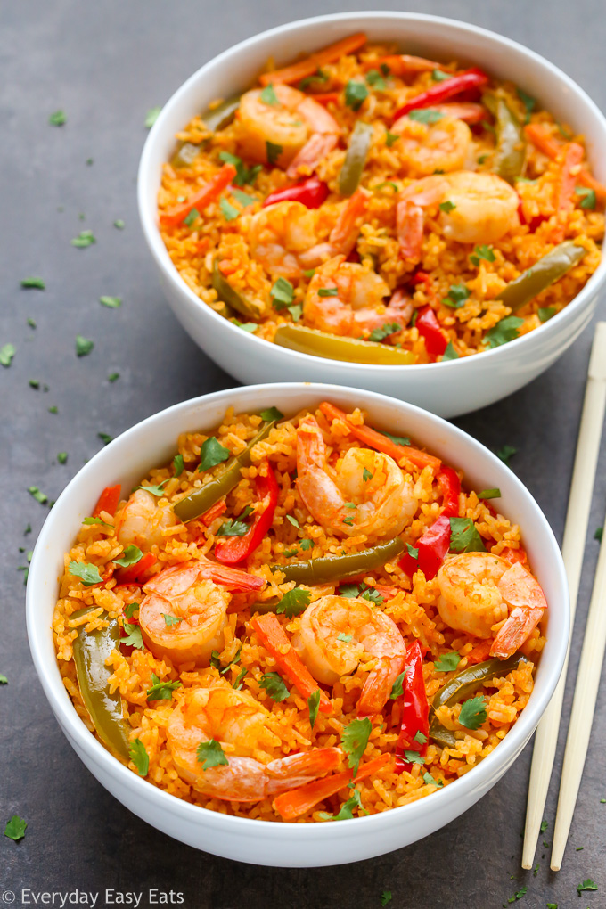 Overhead view of two bowls of Thai Shrimp and Rice with chopsticks on a black surface.