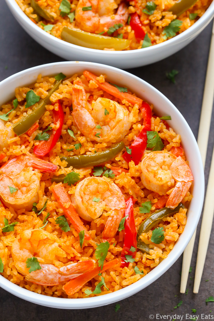 Close-up overhead view of a bowl of Thai Shrimp and Rice with chopsticks on a black surface.