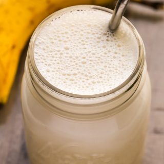 Close-up overhead view of Banana Protein Shake in a glass mason jar with a metal straw inserted on a wooden background.