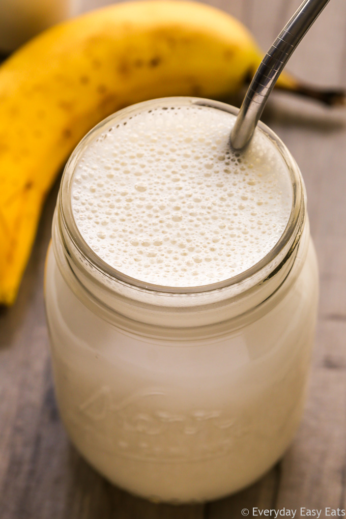 Protein Shake Recipes for Weight Loss: Close-up overhead view of Banana Protein Shake in a glass mason jar with a metal straw inserted on a wooden background.