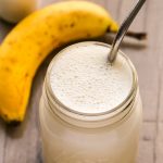 Overhead view of Banana Protein Shake in a glass mason jar with a metal straw inserted on a wooden background.