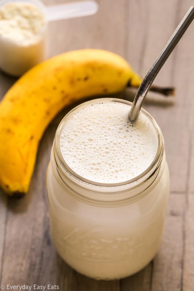 Overhead view of Banana Protein Shake in a glass mason jar with a metal straw inserted on a wooden background.