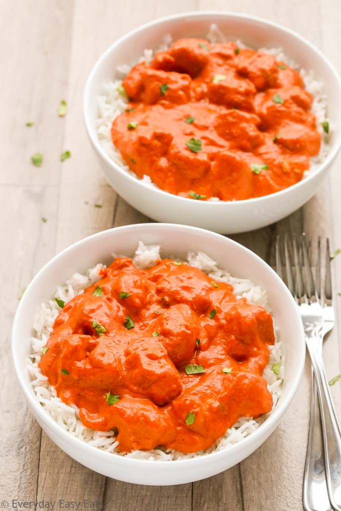 Overhead view of two bowls of Butter Chicken with Curry Paste with white rice on a wooden background.