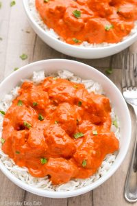 Close-up overhead view of a bowl of Easy Indian Butter Chicken with white rice on a wooden background.