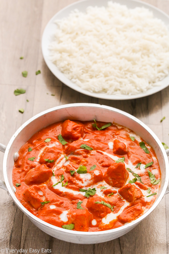 Overhead view of Butter Chicken with Curry Paste in a silver serving bowl with a plate of white rice on a wooden background.