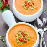 Side overhead view of Spicy Thai Pumpkin Soup in white bowls with spoons on black background.