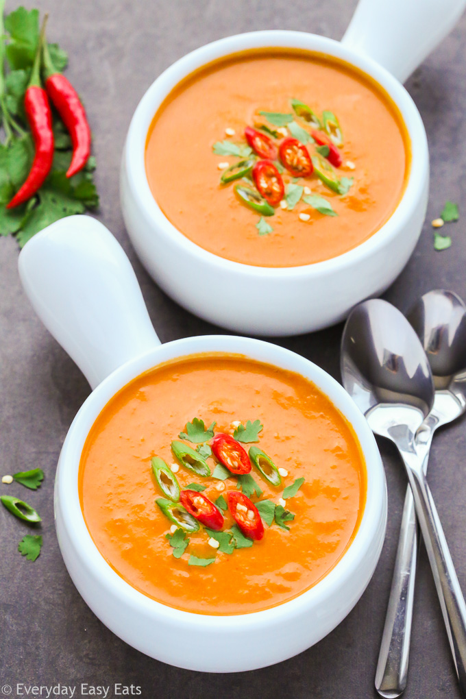 Side overhead view of Spicy Thai Pumpkin Soup in white bowls with spoons on black background.