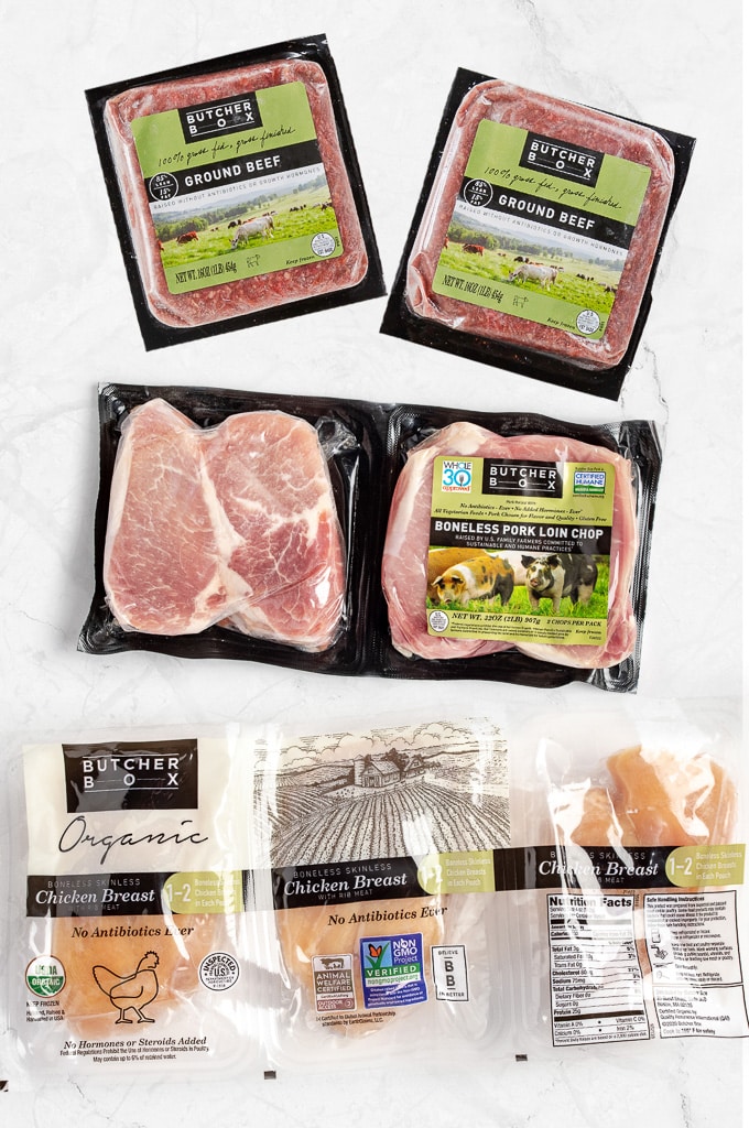 Honest ButcherBox Review: Packages of frozen grass-fed ground beef, pork loin chops, and organic chicken breasts on a white marble table.