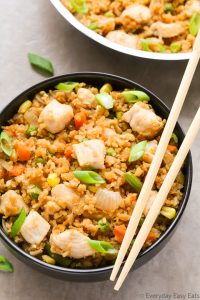 Close-up overhead view of a bowl of Healthy Chicken Fried Rice with chopsticks on the side on a neutral background.