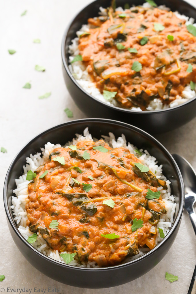 Close-up overhead view of two bowls of Coconut Lentil Curry with spoons on the side on a neutral background.