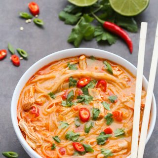 Side overhead view of Thai Chicken Noodle Soup in a white bowl with chopsticks on a dark background.