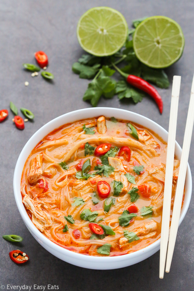 Side overhead view of Thai Chicken Noodle Soup in a white bowl with chopsticks on a dark background.