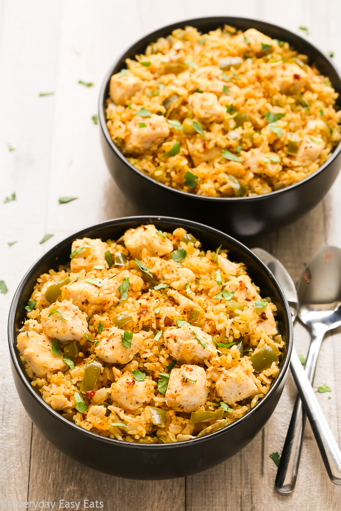 Overhead view of two bowls of Cajun Chicken and Rice on a beige background with two spoons on the side..