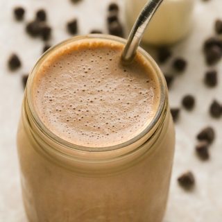 Overhead view of a Chocolate Protein Shake in a glass jar with a metal straw on a neutral background.