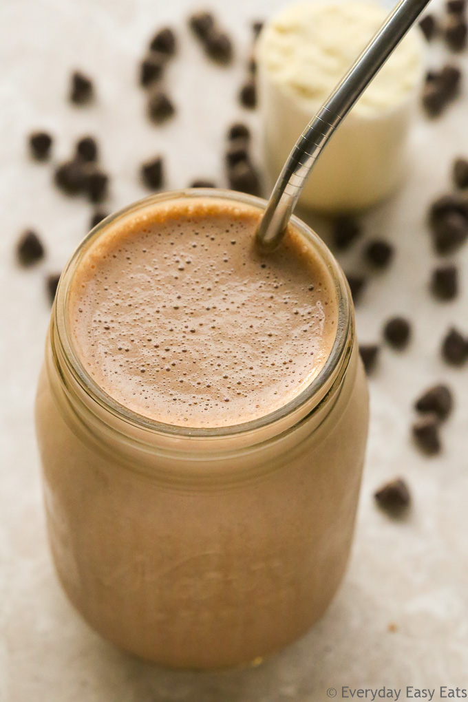 Overhead view of a Chocolate Protein Shake in a glass jar with a metal straw on a neutral background.