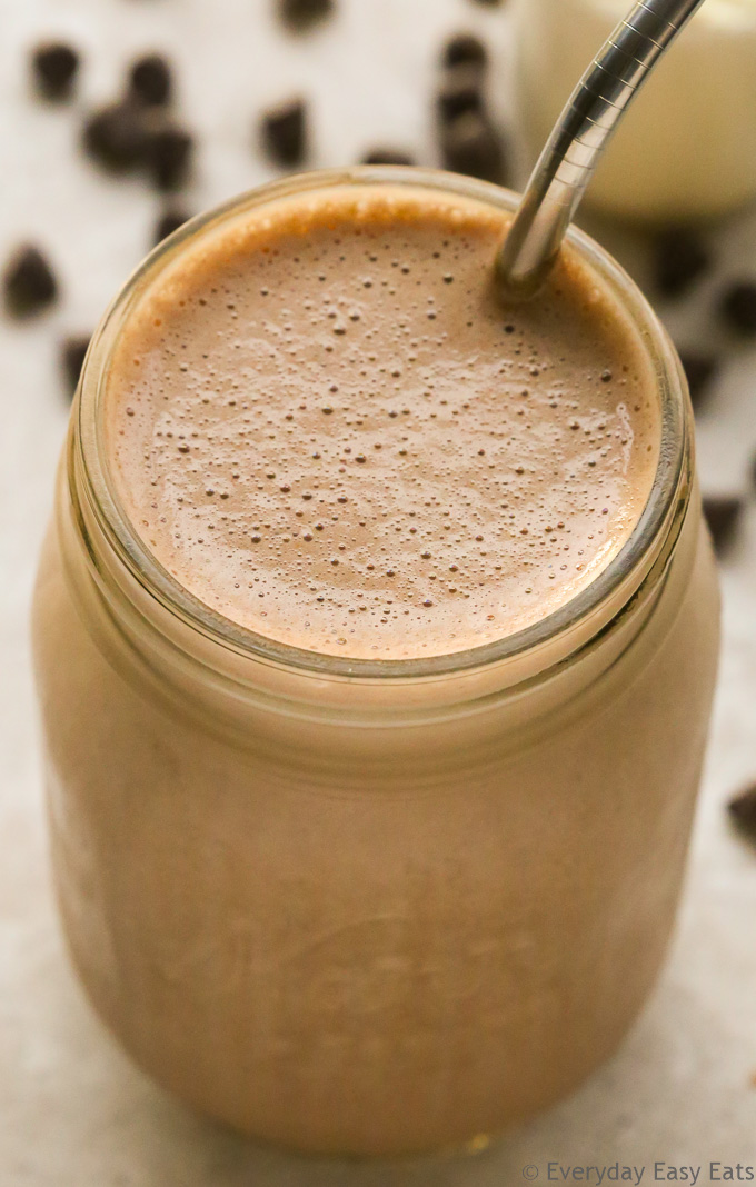 Close-up overhead view of a Chocolate Protein Shake in a glass jar with a metal straw on a neutral background.