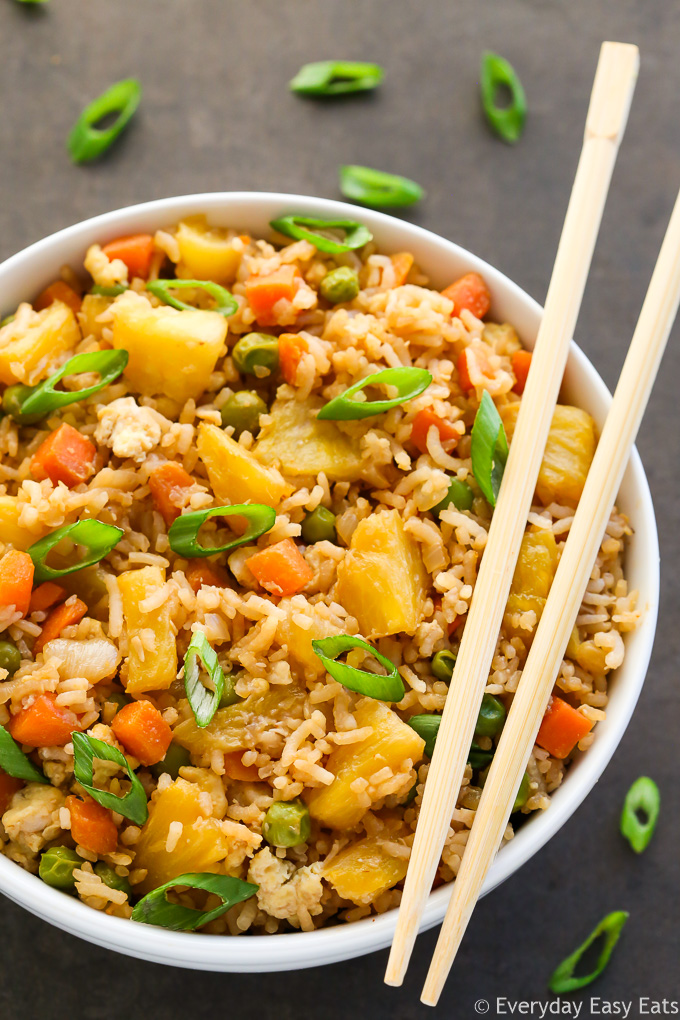 Overhead view of a bowl of Pineapple Fried Rice with chopsticks on the side on a dark background.
