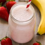 Close-up overhead view of a Strawberry Protein Shake in a glass jar with a straw on a wooden background.