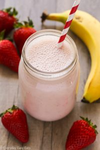 Close-up overhead view of a Strawberry Protein Shake in a glass jar with a straw on a wooden background.