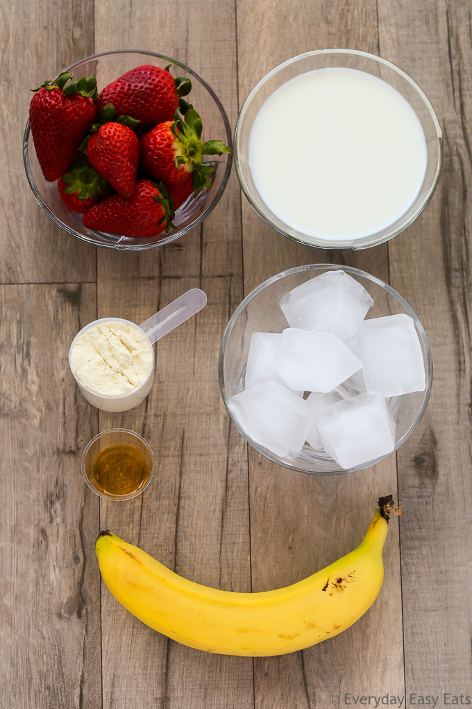 Overhead view of ingredients required to make Strawberry Protein Shake on a wooden background.