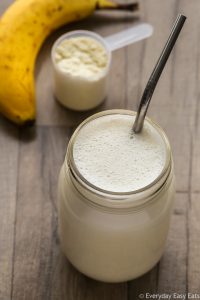 Overhead view of a Vanilla Protein Shake in a glass jar with a metal straw on a wooden background.