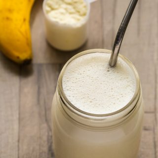 Overhead view of a Whey Protein Shake in a glass jar with a metal straw on a wooden background.