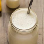 Close-up overhead view of a Vanilla Protein Shake in a glass jar with a metal straw on a wooden background.