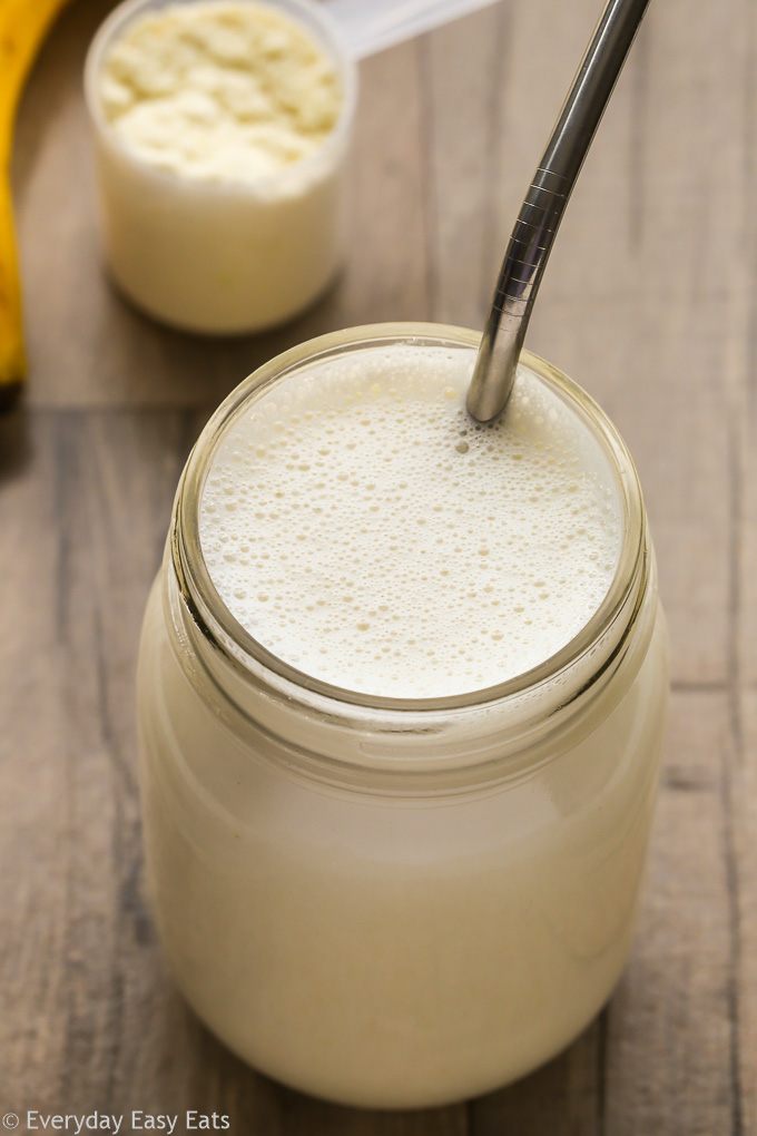 Close-up overhead view of a Vanilla Protein Shake in a glass jar with a metal straw on a wooden background.