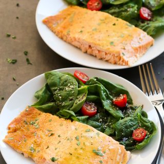Side overhead view of two pieces of Healthy Baked Honey Mustard Salmon in white plates with salad on the side.