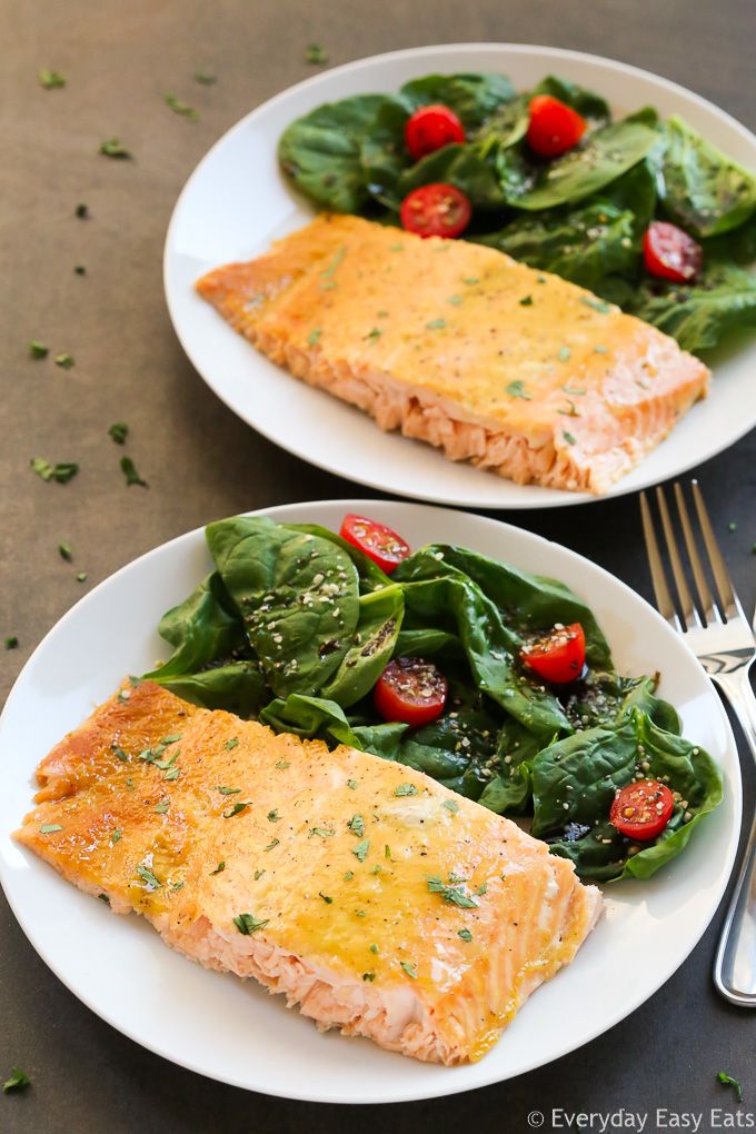 Side overhead view of two pieces of Baked Honey Mustard Salmon in white plates with salad on the side.