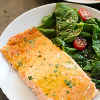 Close-up overhead view of a piece of Baked Honey Mustard Salmon in a white plate with salad on the side.