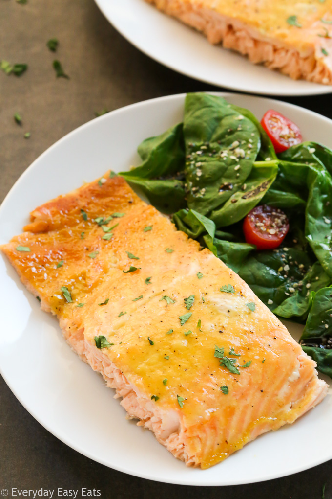 Close-up overhead view of a piece of Healthy Baked Honey Mustard Salmon in a white plate with salad on the side.