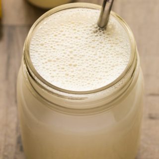 Close-up overhead view of a Vegan Protein Shake in a glass jar with a metal straw on a wooden background.