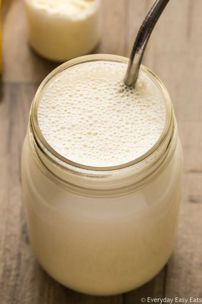 Close-up overhead view of a Vegan Protein Shake in a glass jar with a metal straw on a wooden background.