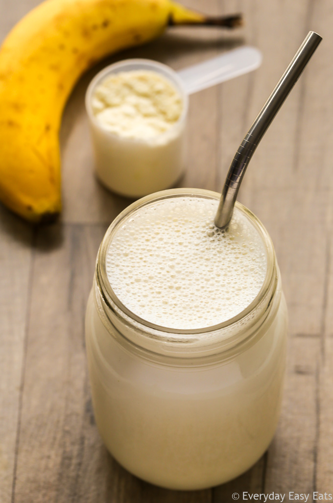 Overhead view of a Vegan Protein Shake in a glass jar with a metal straw on a wooden background.