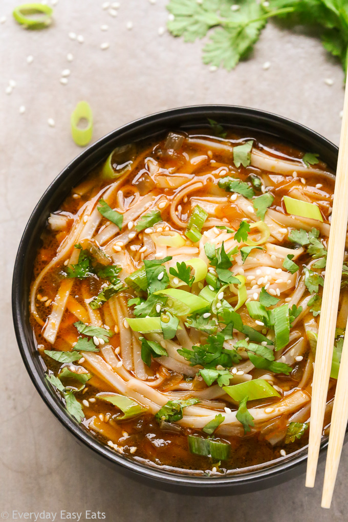 Close-up overhead view of Spicy Asian Noodle Soup in a black bowl with chopsticks on a neutral background.