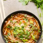 Overhead view of Asian Spicy Noodle Soup in a black bowl on a neutral background.