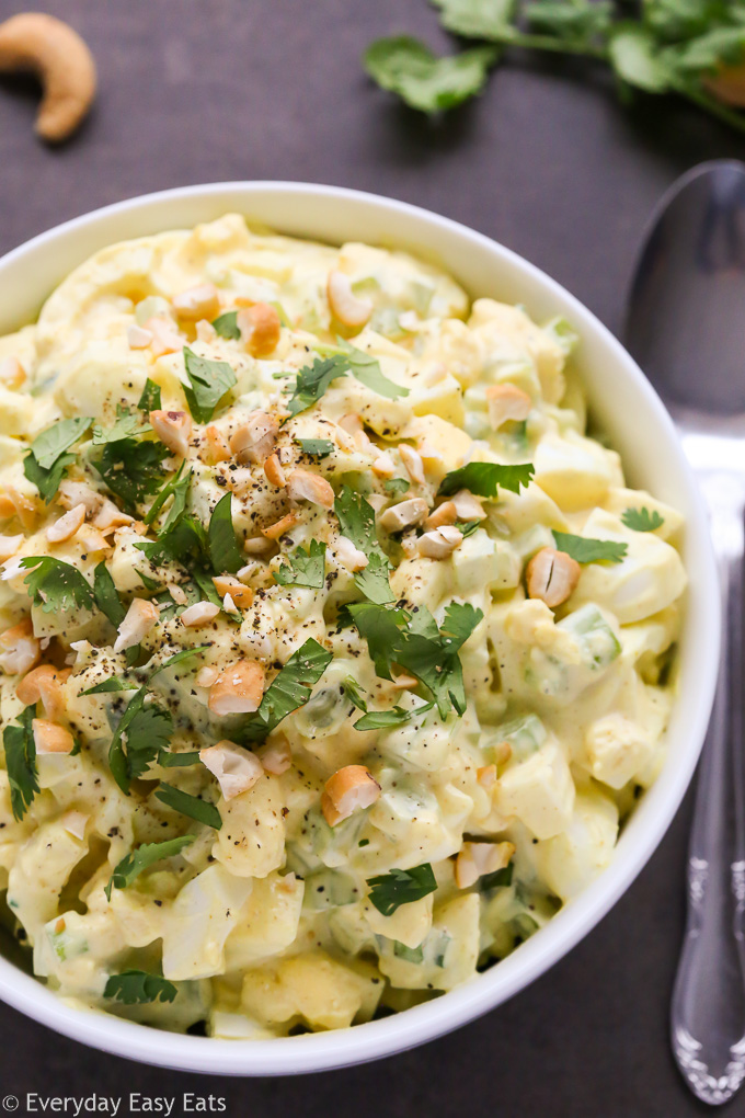 Close-up overhead view of Curried Egg Salad in a white bowl on a black surface.