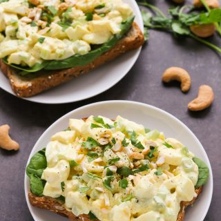 Overhead view of two Curried Egg Salad Sandwiches in white plates on a black surface.