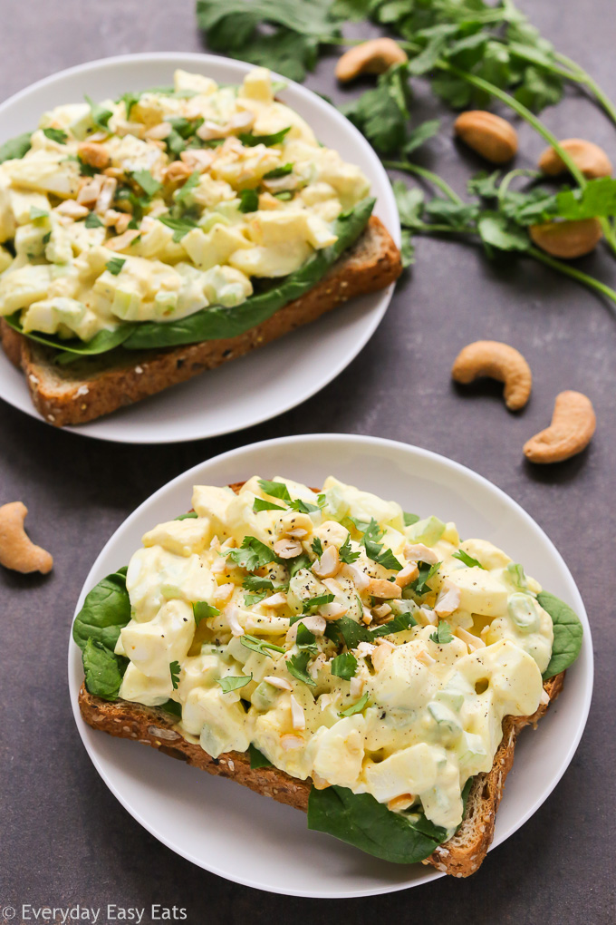 Overhead view of two Curried Egg Salad Sandwiches in white plates on a black surface.