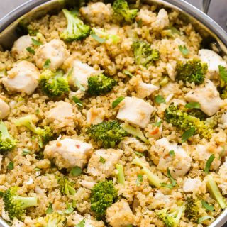 Close-up overhead view of Chicken Broccoli Quinoa in a silver skillet on a black surface.